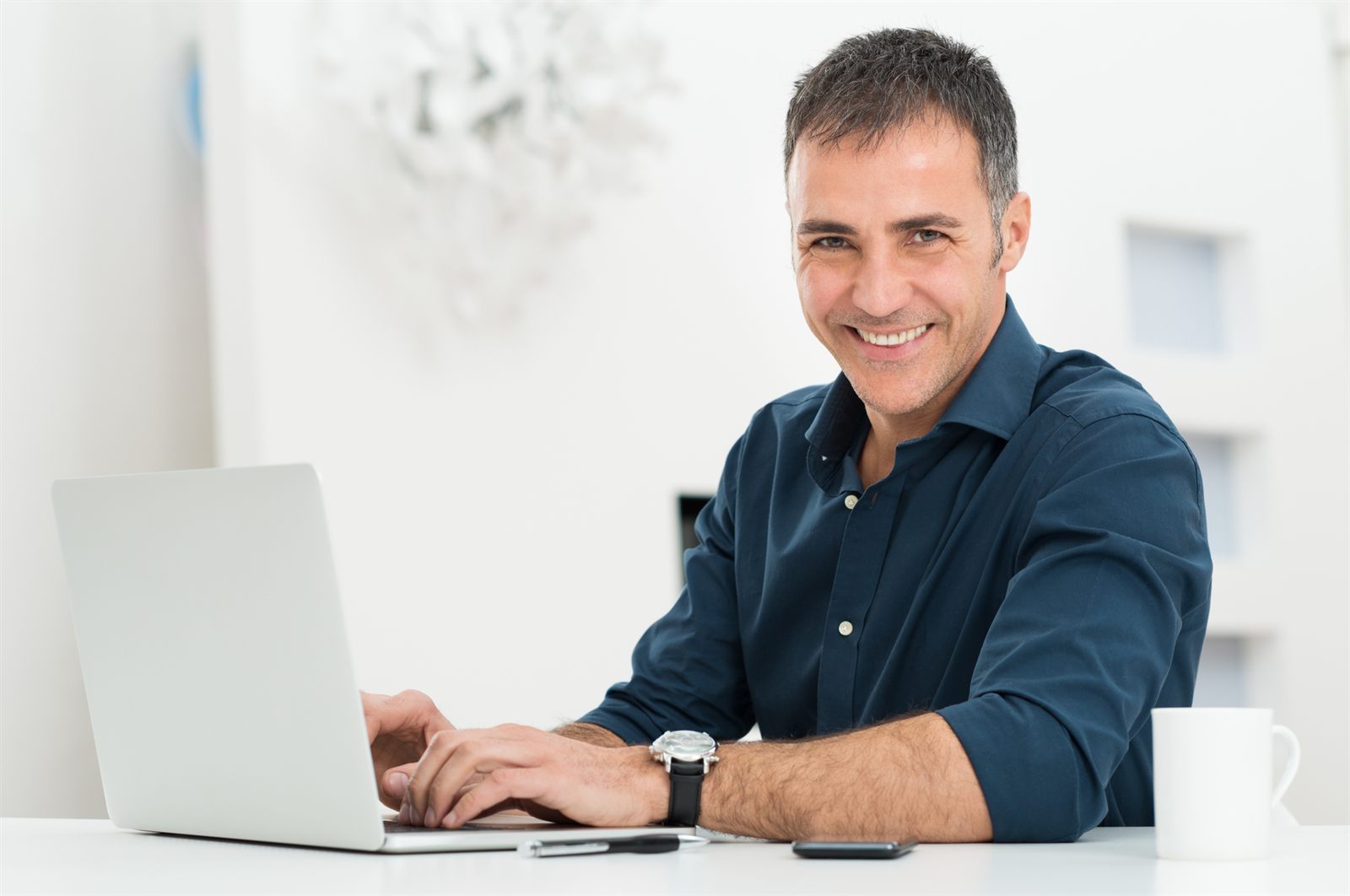 Man smiling while working on a laptop at a bright desk