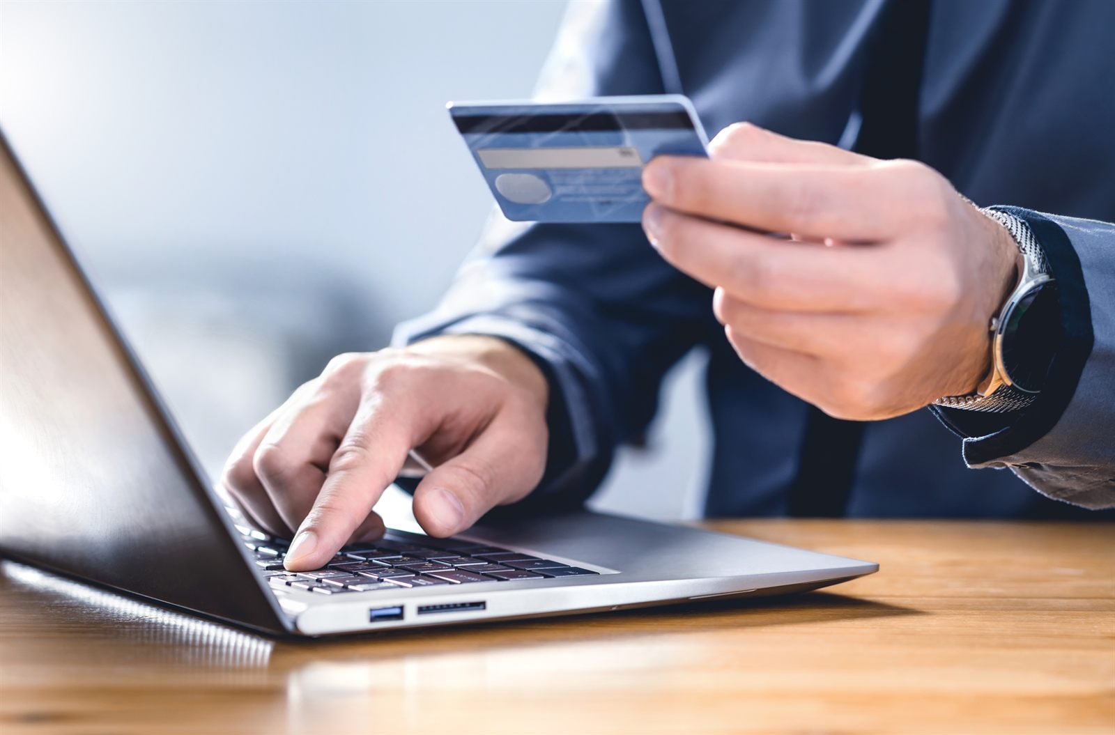 Person holding a payment card while typing on a laptop